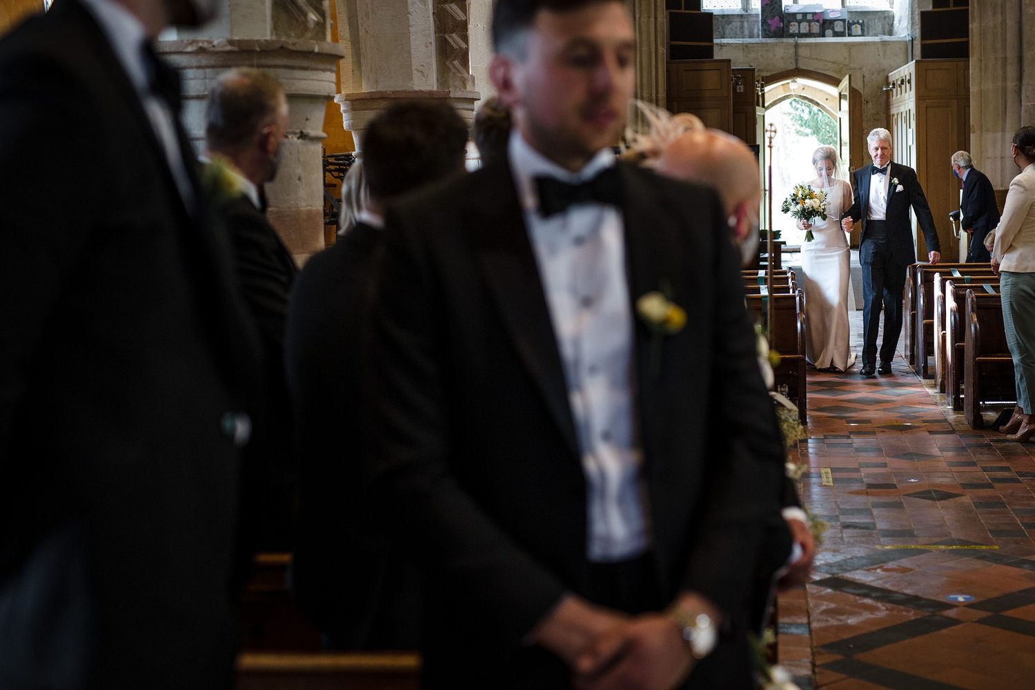 Guests stand in a church aisle during a wedding ceremony, with the bride and groom visible at the altar.