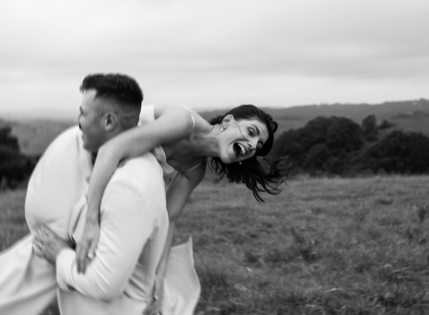 A playful black and white photo of a couple laughing together in a meadow.