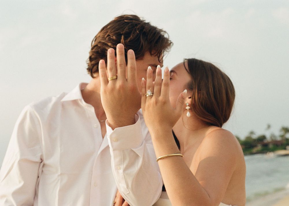 Couple kissing on beach showing off engagement rings, tropical destination proposal photo.