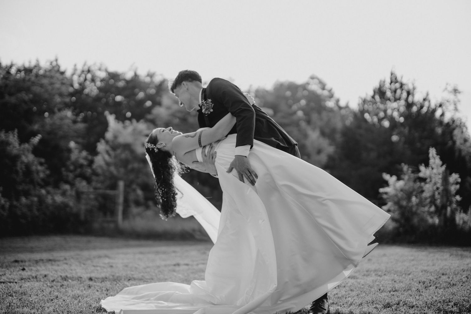 Black and white photo of a groom dipping his bride in a romantic outdoor wedding dance pose.