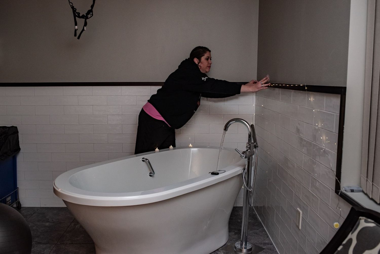 doula reaching to adjust lights over a freestanding white bathtub.