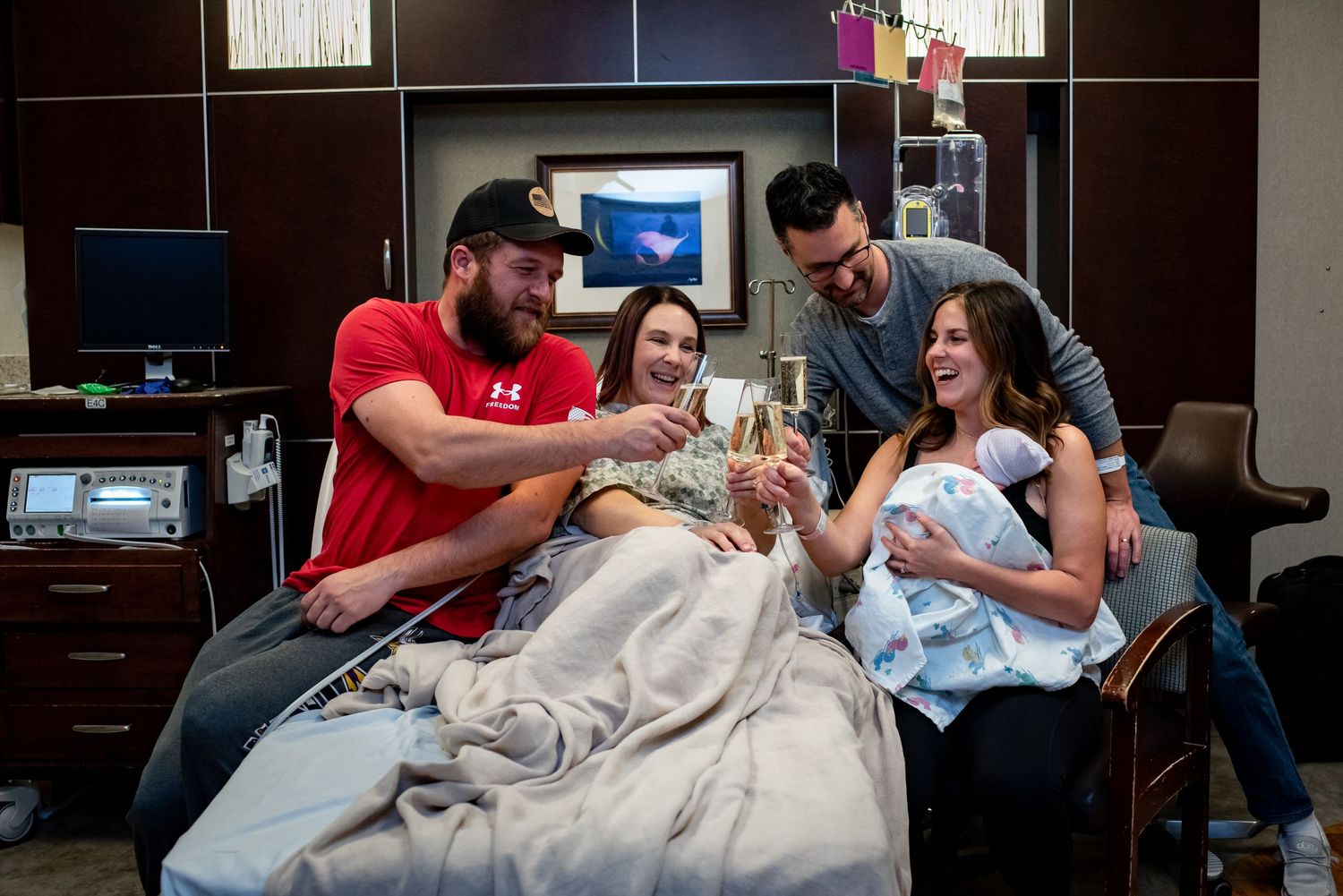 Group celebrates in hospital room with drinks while gathered around new baby.