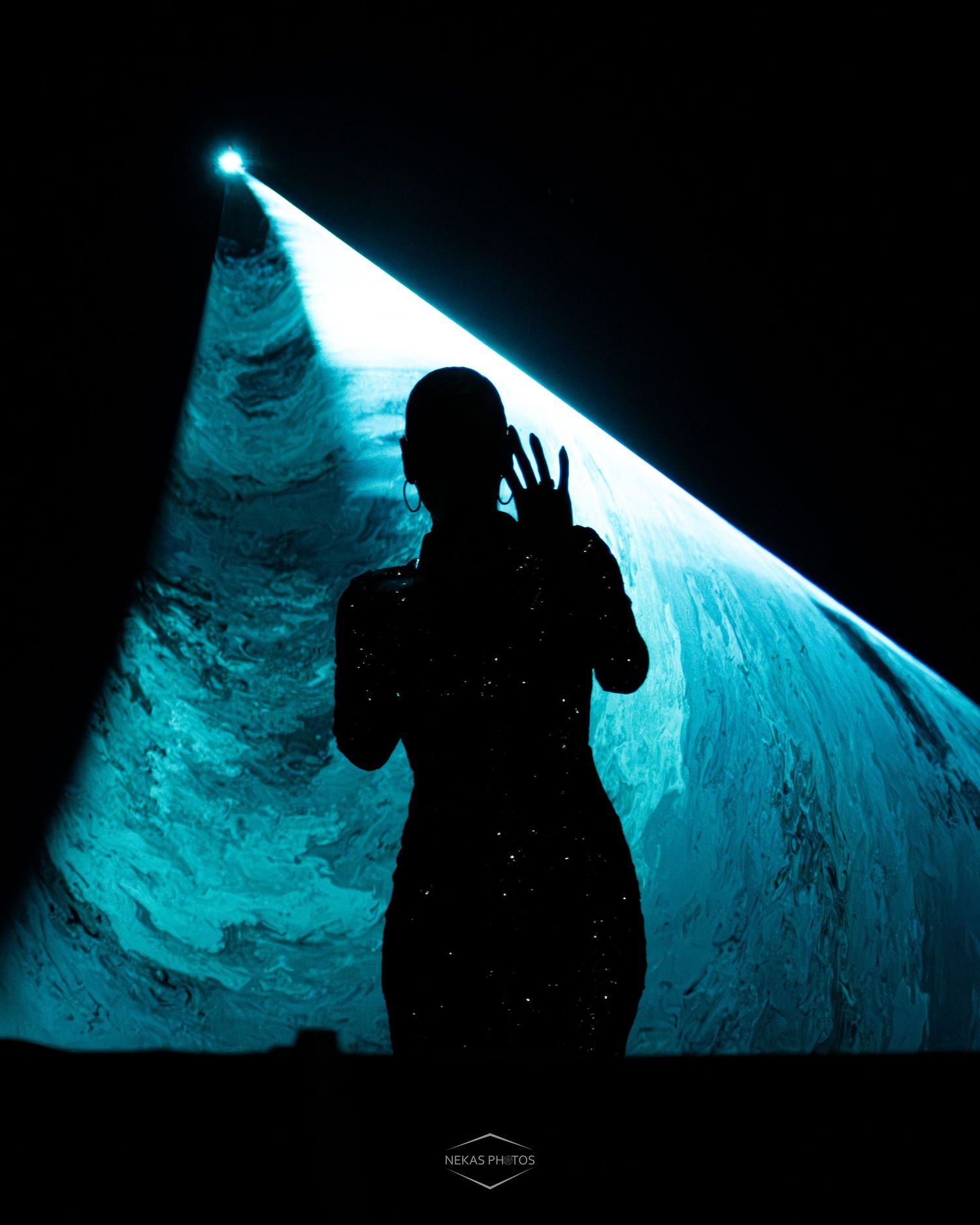 A female performer in a sequined black gown sings passionately on stage under dramatic blue lighting.