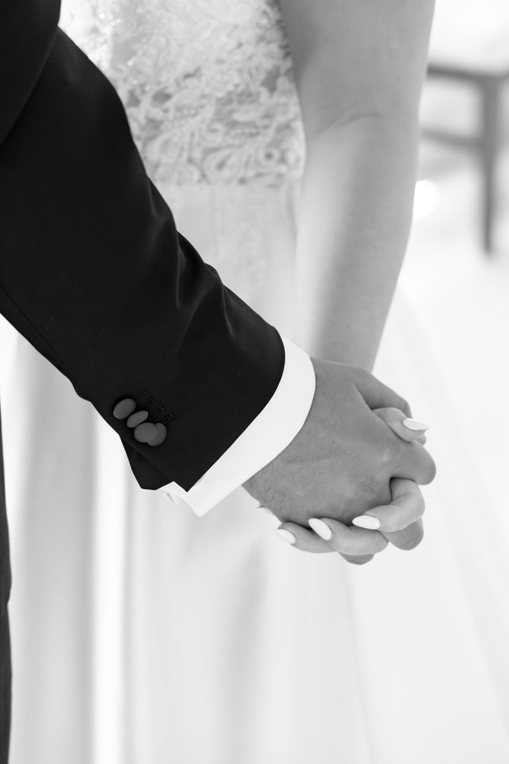 Bride and groom holding hands in black and white wedding photo closeup.