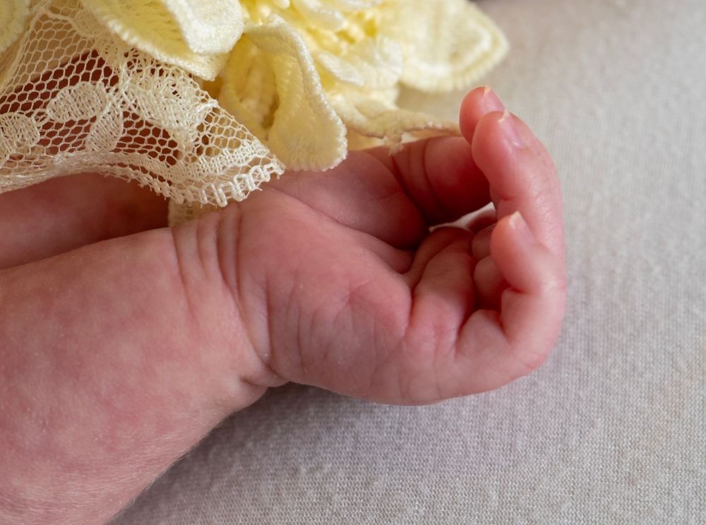 Close-up of a newborn baby's tiny hand wearing a delicate yellow lace dress.
