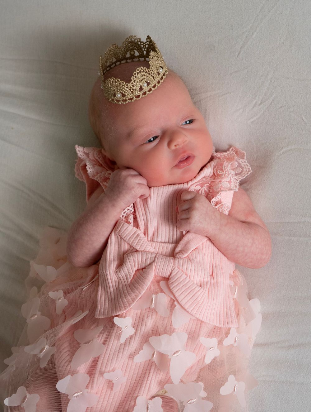 Newborn baby girl in pink ruffled dress wearing a gold lace crown.