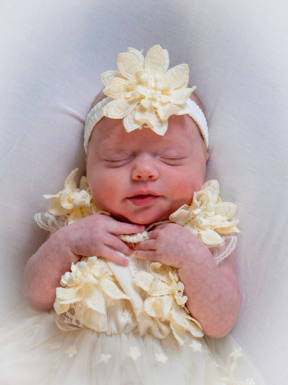 Sleeping newborn baby girl in cream lace dress with floral headband.