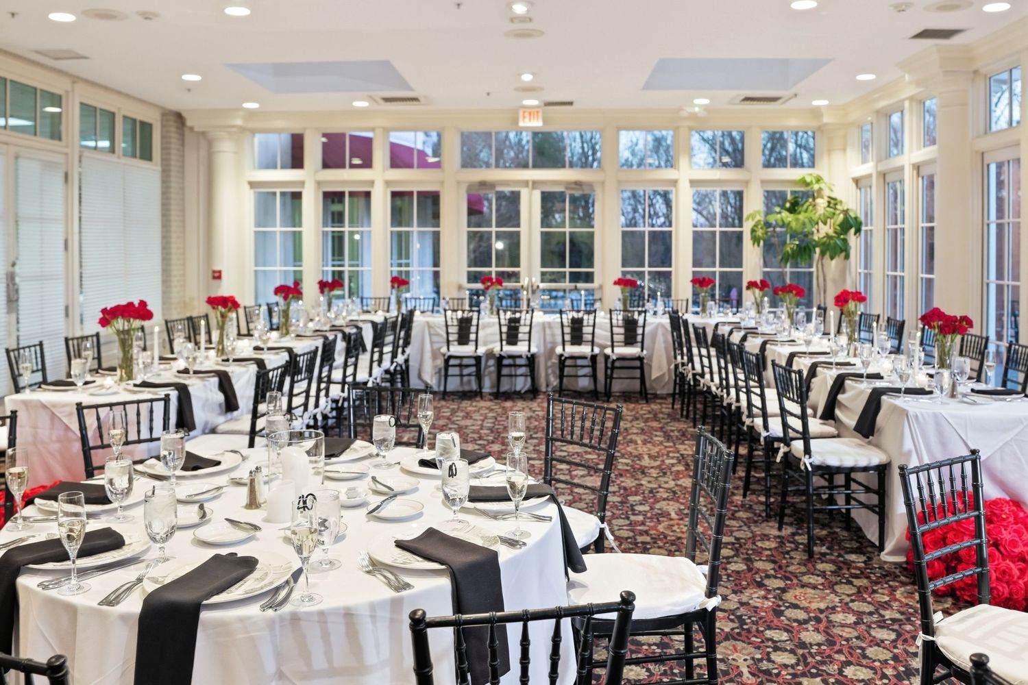 Deerfield Golf Club Newark white-draped round tables, black chairs, red floral centerpieces, and large windows flooding the room with light.