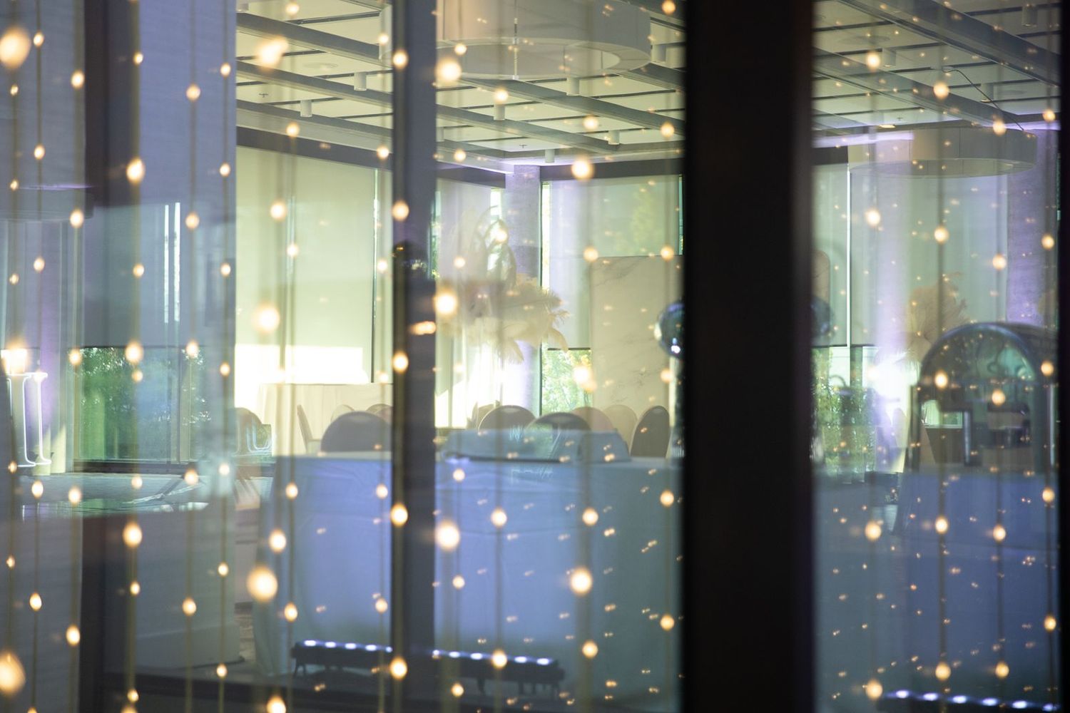 Warm glowing lights reflected on glass windows of an elegant indoor wedding venue.