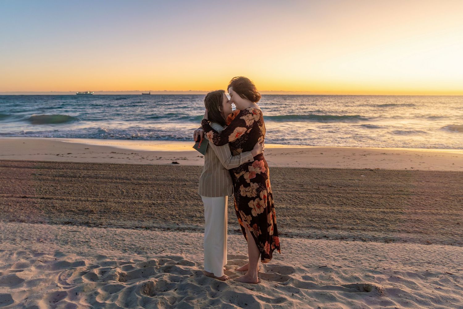 Couple embracing and kissing on a sandy beach at golden sunset with ocean waves in the background.