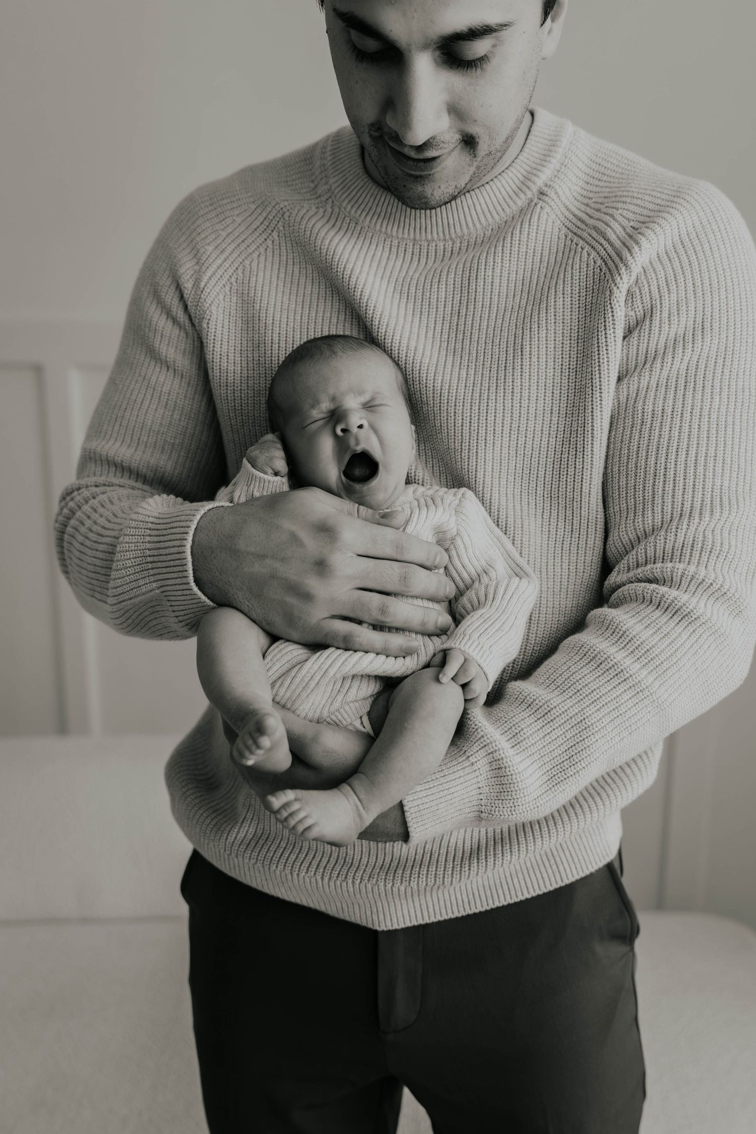 Close-up black and white photo of tiny newborn baby feet peeking out from a soft white knit blanket.