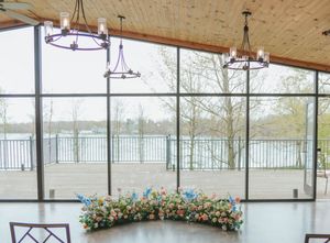 Elegant wedding venue with floor-to-ceiling windows, lake views, floral centerpiece, and rustic chandeliers.