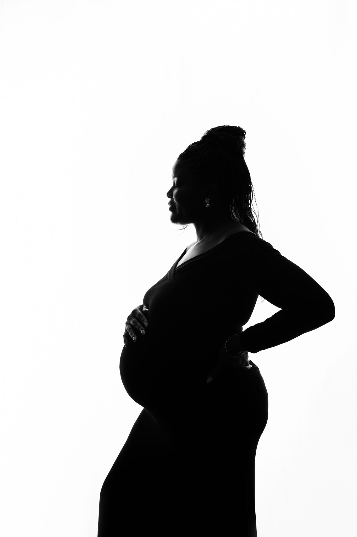 Black and white silhouette of a pregnant woman cradling her baby bump against a white background.