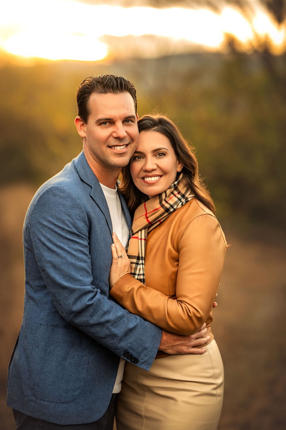 Smiling couple embracing outdoors at sunset wearing blue blazer and Burberry scarf for photos with Marietta photographer.
