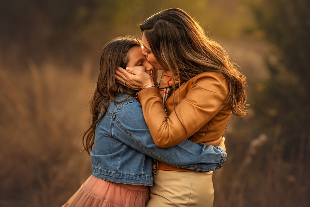 A mother and young daughter share a tender forehead-to-forehead embrace outdoors in a warm autumn field.