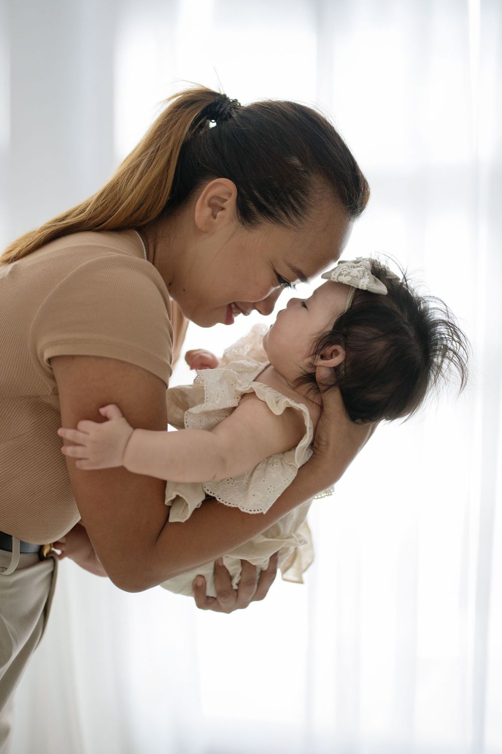 A mother tenderly touches foreheads with her newborn baby girl in a bright, softly lit room.