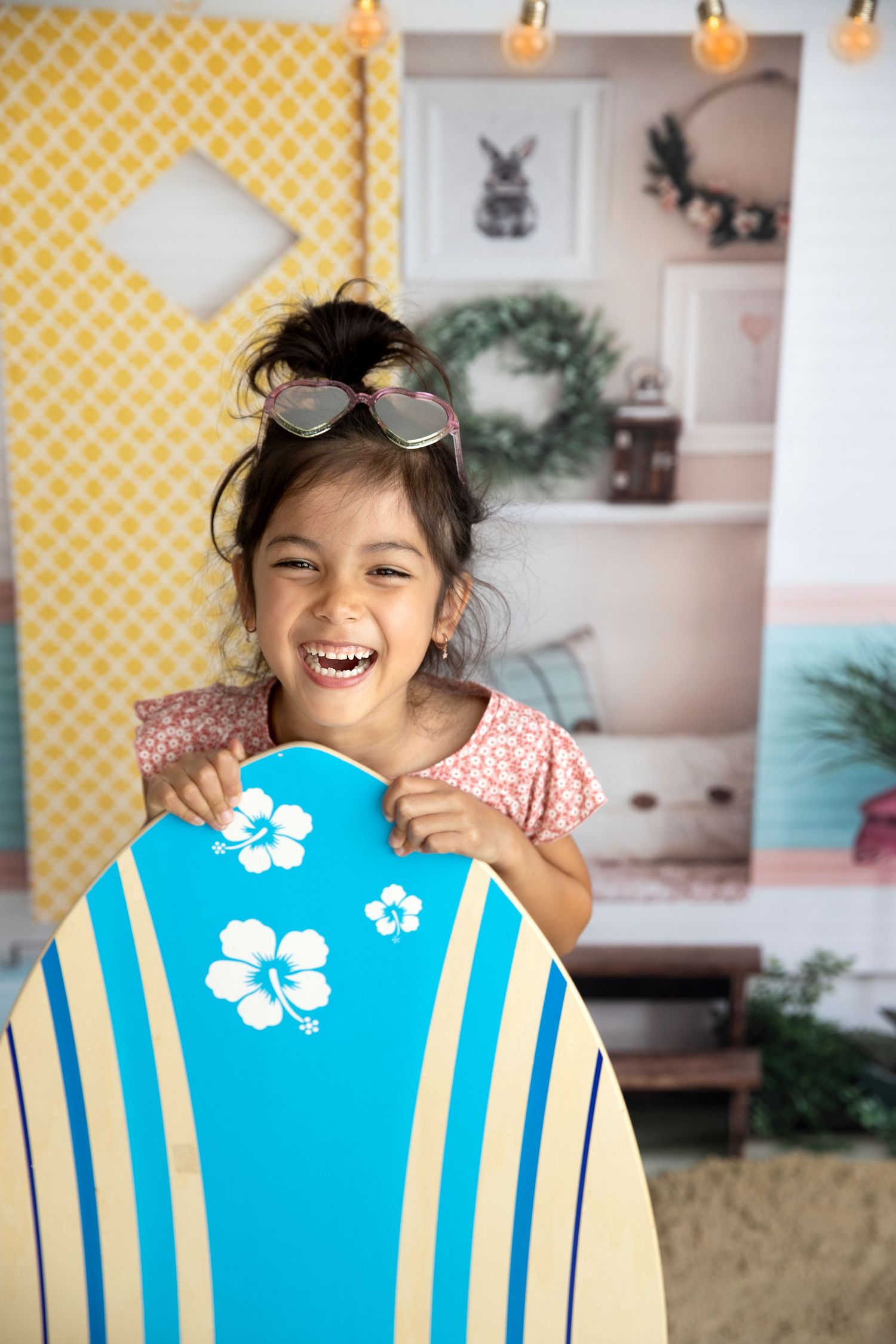 Happy young girl laughing while holding a blue and yellow surfboard with hibiscus flowers indoors. Beach Summer Photography Photos Cork