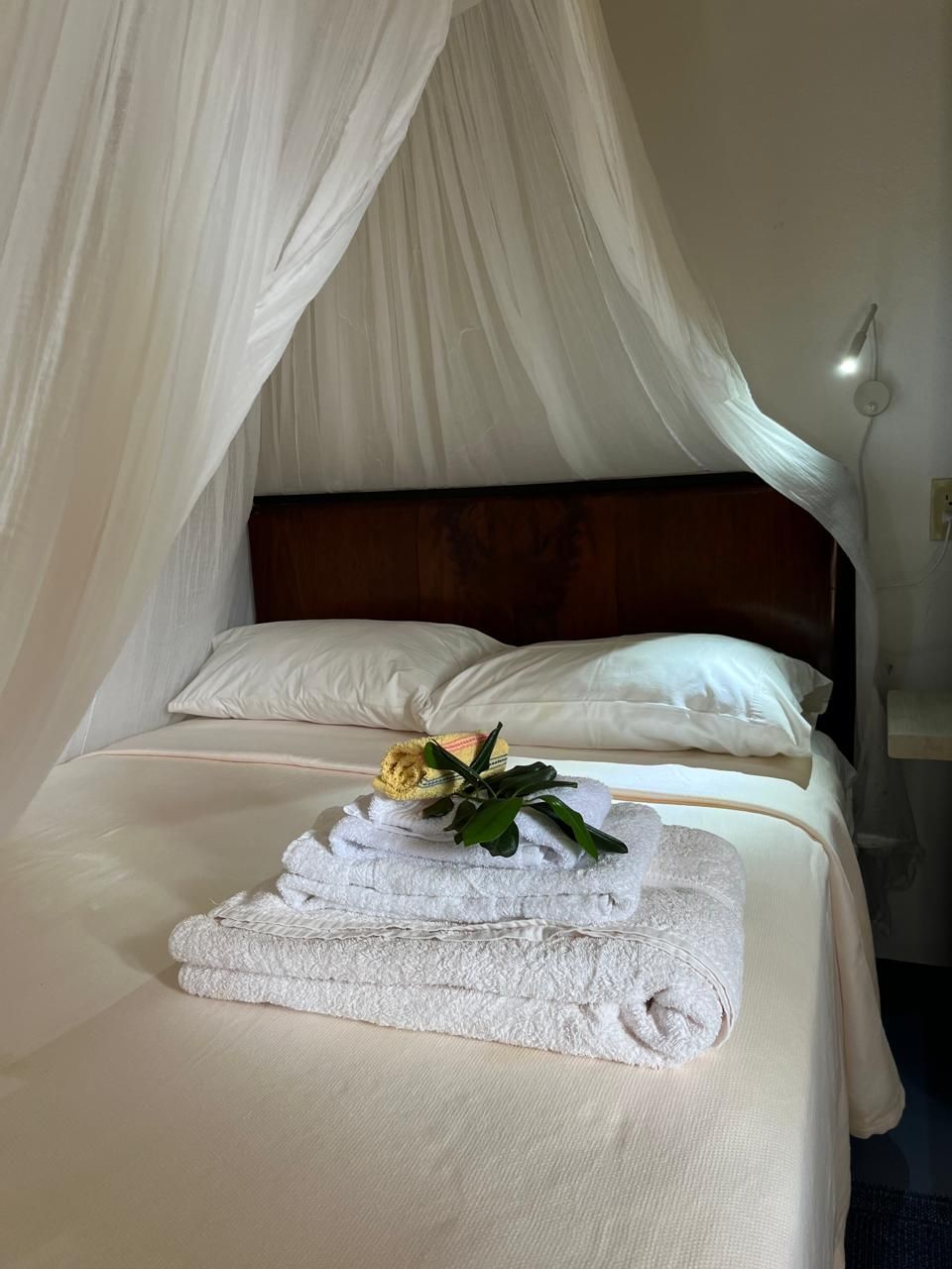 Elegant canopy bed with white draping, crisp linens, folded towels, and a yellow rose in a cozy hotel bedroom.