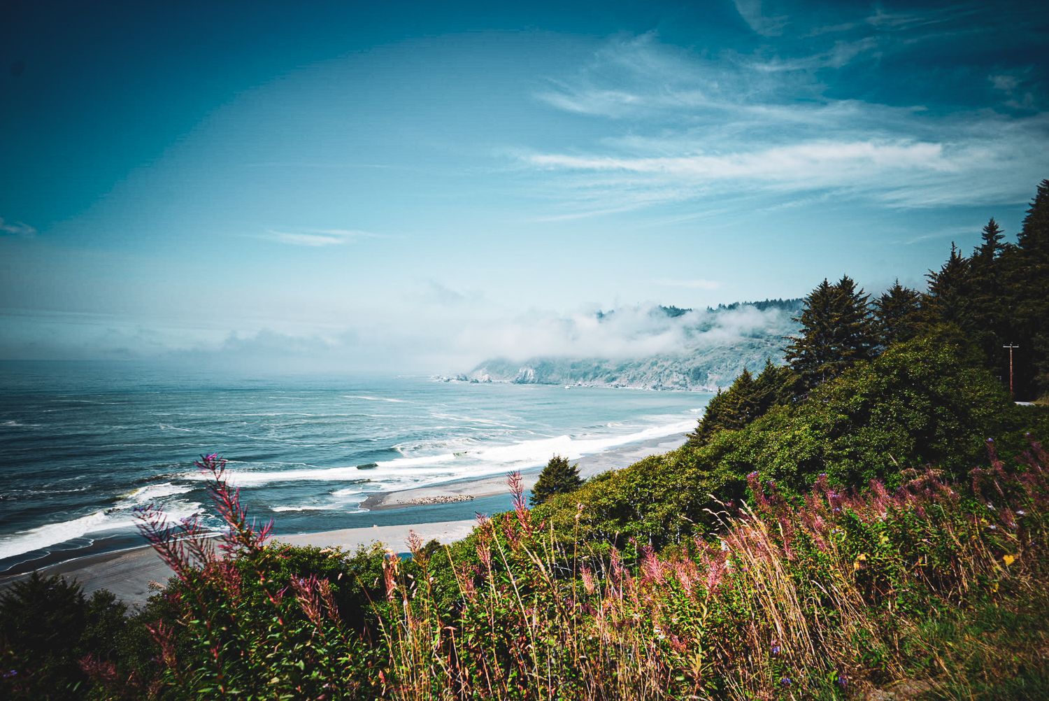 Misty coastal cliffs with rocky shoreline and crashing waves under a foggy sky along a scenic coastline.