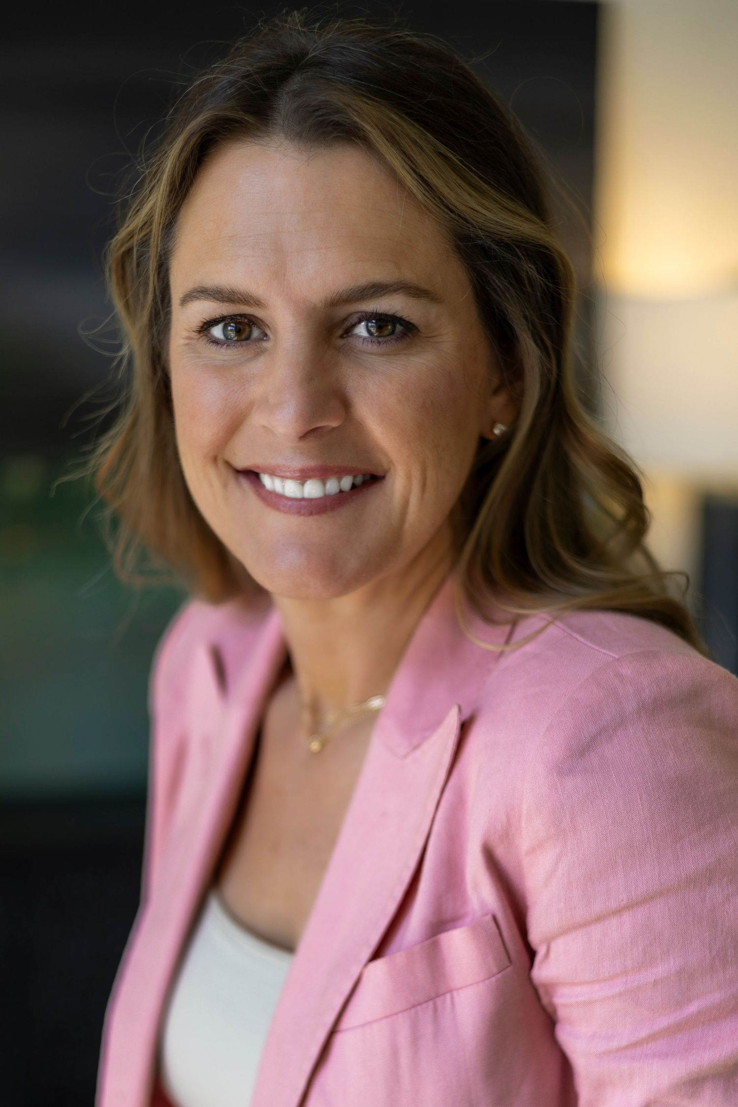 Smiling professional woman in a pink blazer poses for a business portrait with a warm, confident expression.