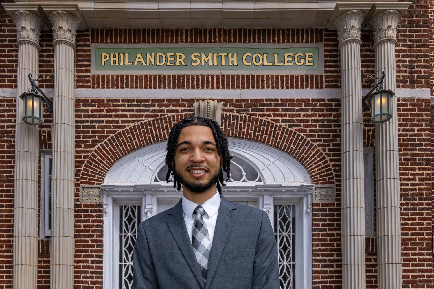 Young man in suit smiling in front of Philander Smith College brick building entrance.