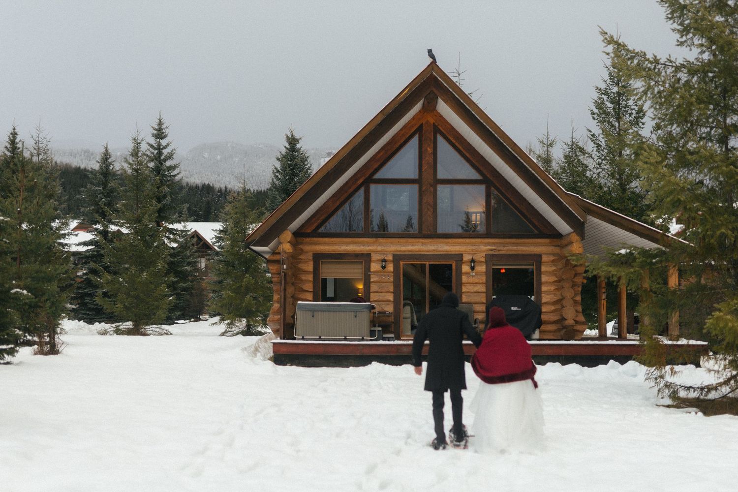 bride and groom snowshoe toward a log cabin