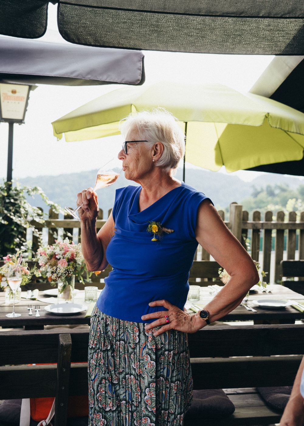 eine Dame steht im Gastgarten des Hochzeitslokals und trinkt genüsslich ein Glas Prosecco