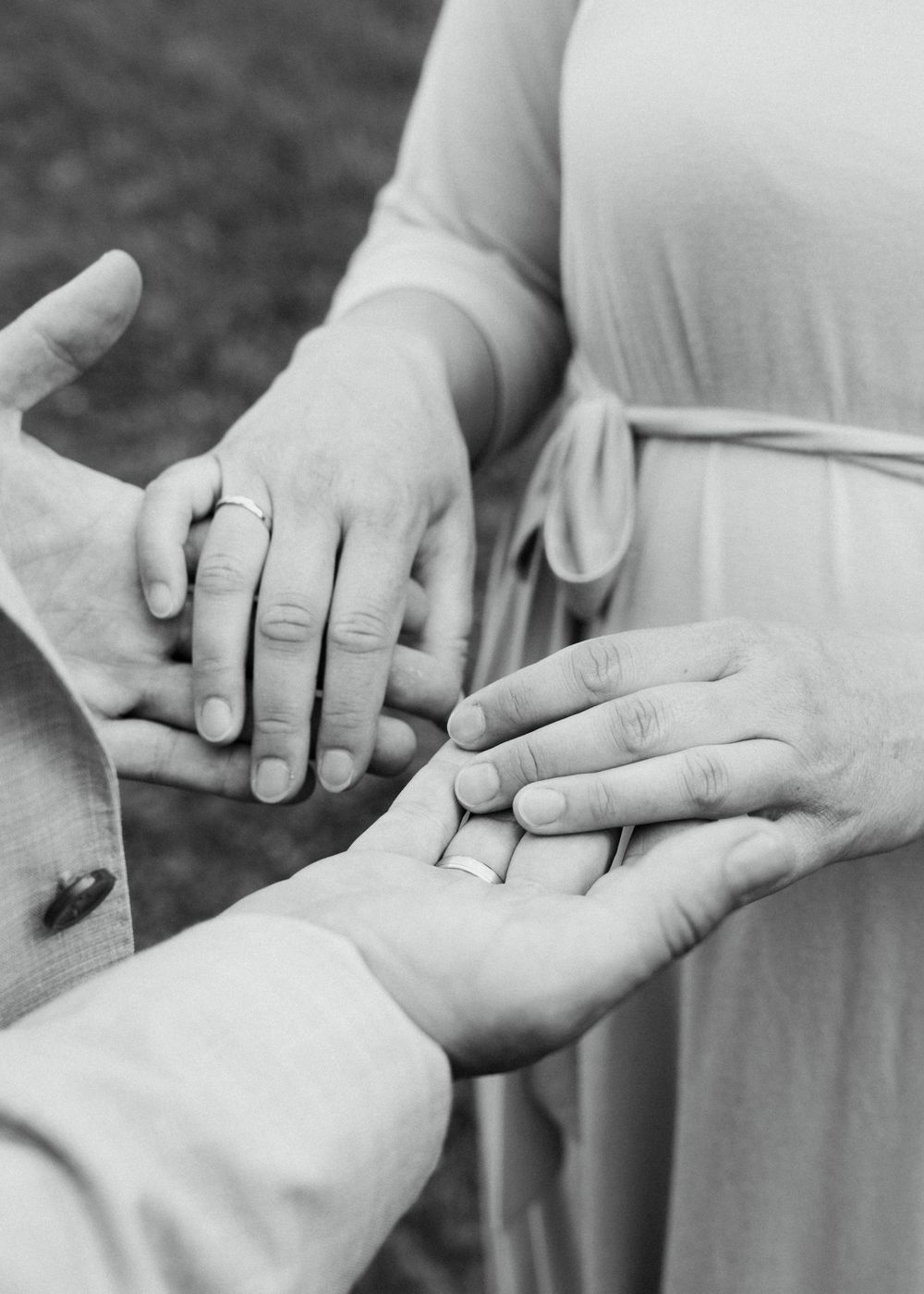 Hochzeitsfotografie, Detailaufnahme, schwarz-weißes Bild, zwei Handpaare die sich berühren, weicher Bildlook, Eheringe zu erkenne