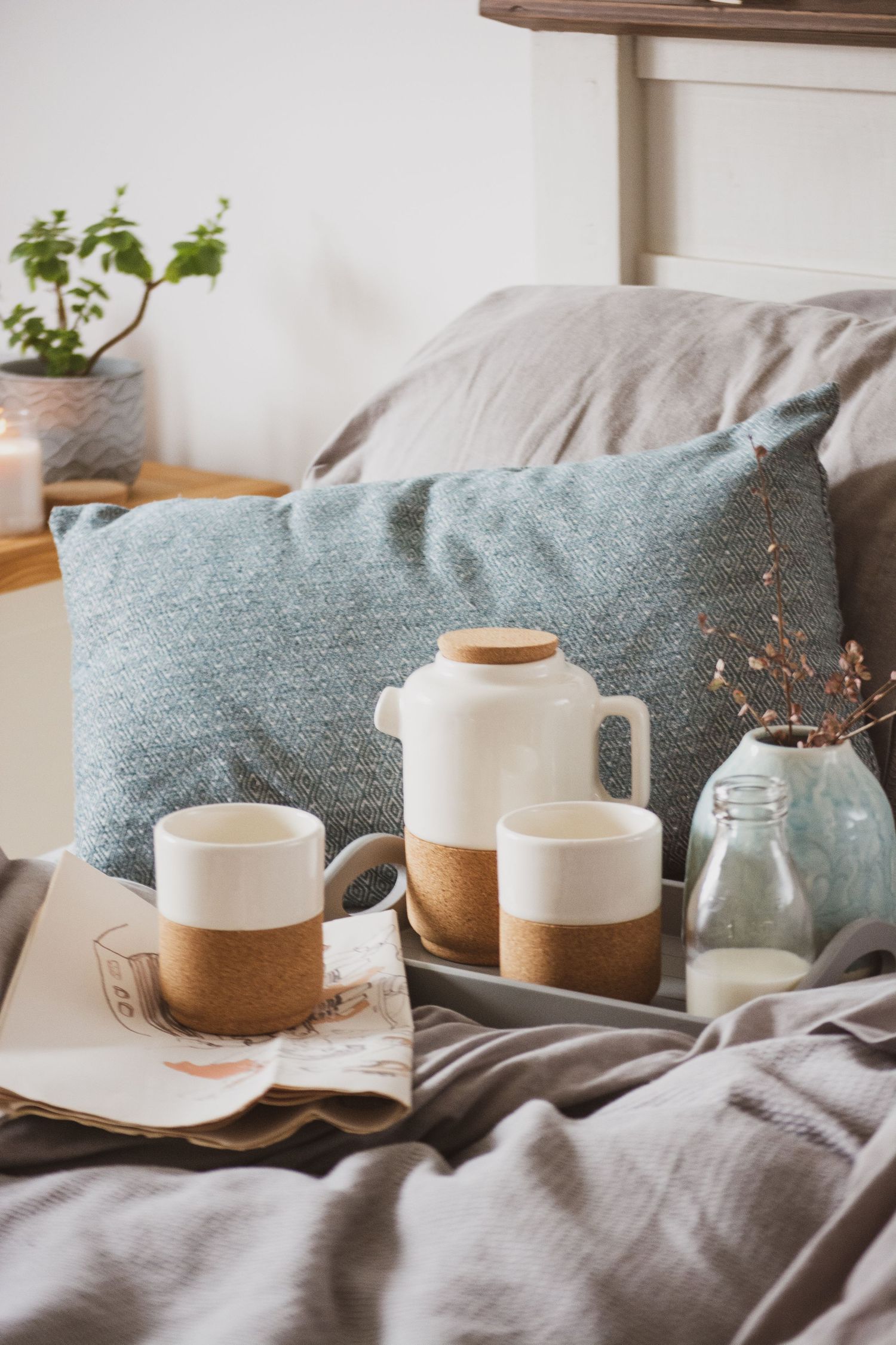 lifestyle photo of an eco teapot and cups on a bed with newspaper, milk bottle and foliage on grey bedding