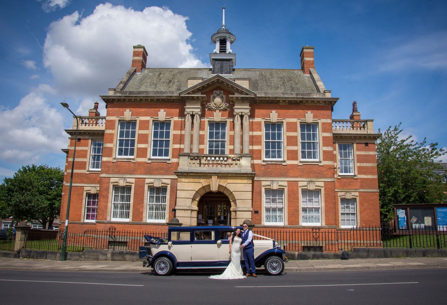 Classic vintage car parked in front of elegant red brick building with ornate architecture.