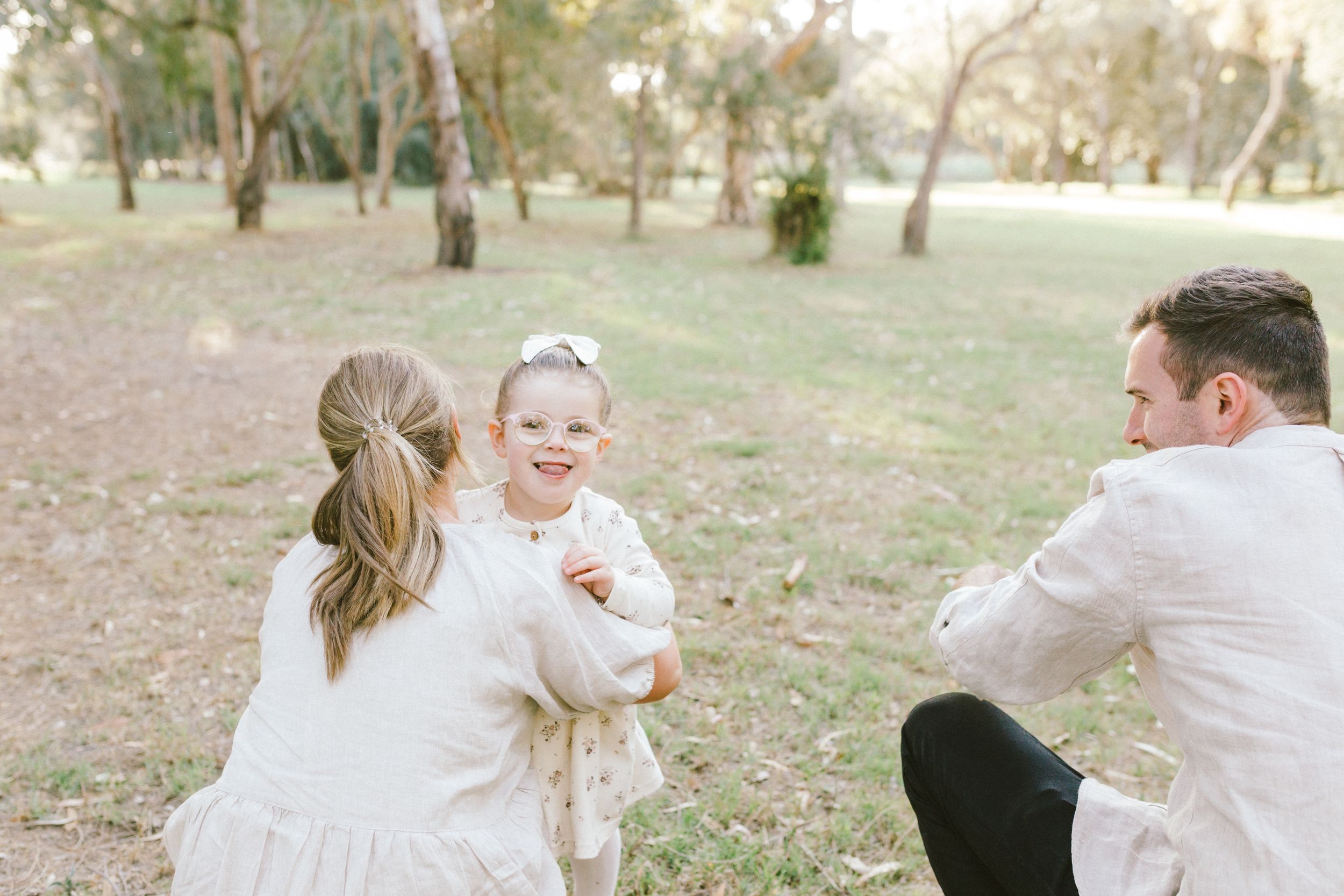 Family enjoying a casual outdoor photo session in a natural park setting with soft lighting and neutral attire.