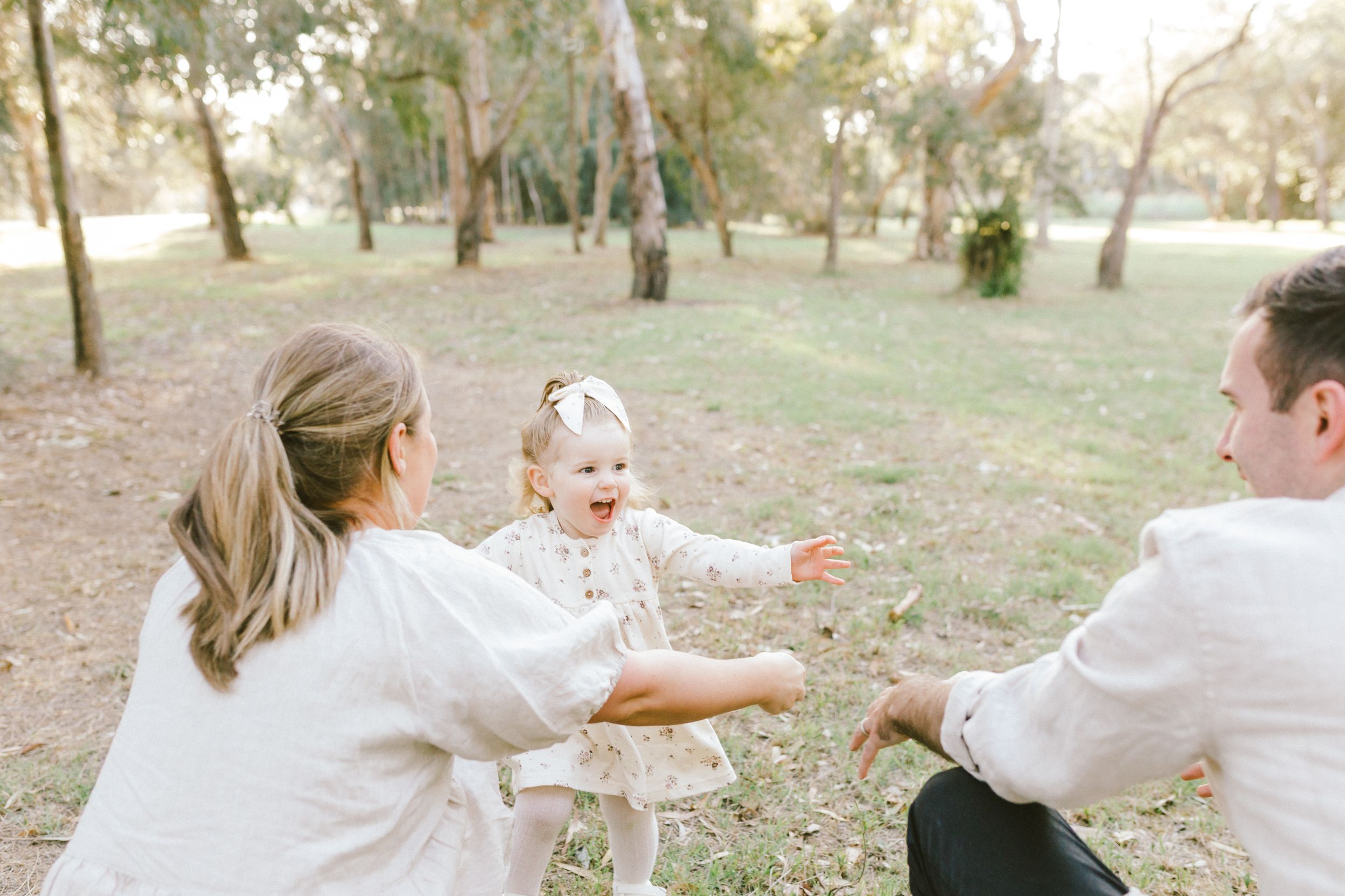 A group in white clothing poses playfully in a sunny park setting under tall trees during a summer day.