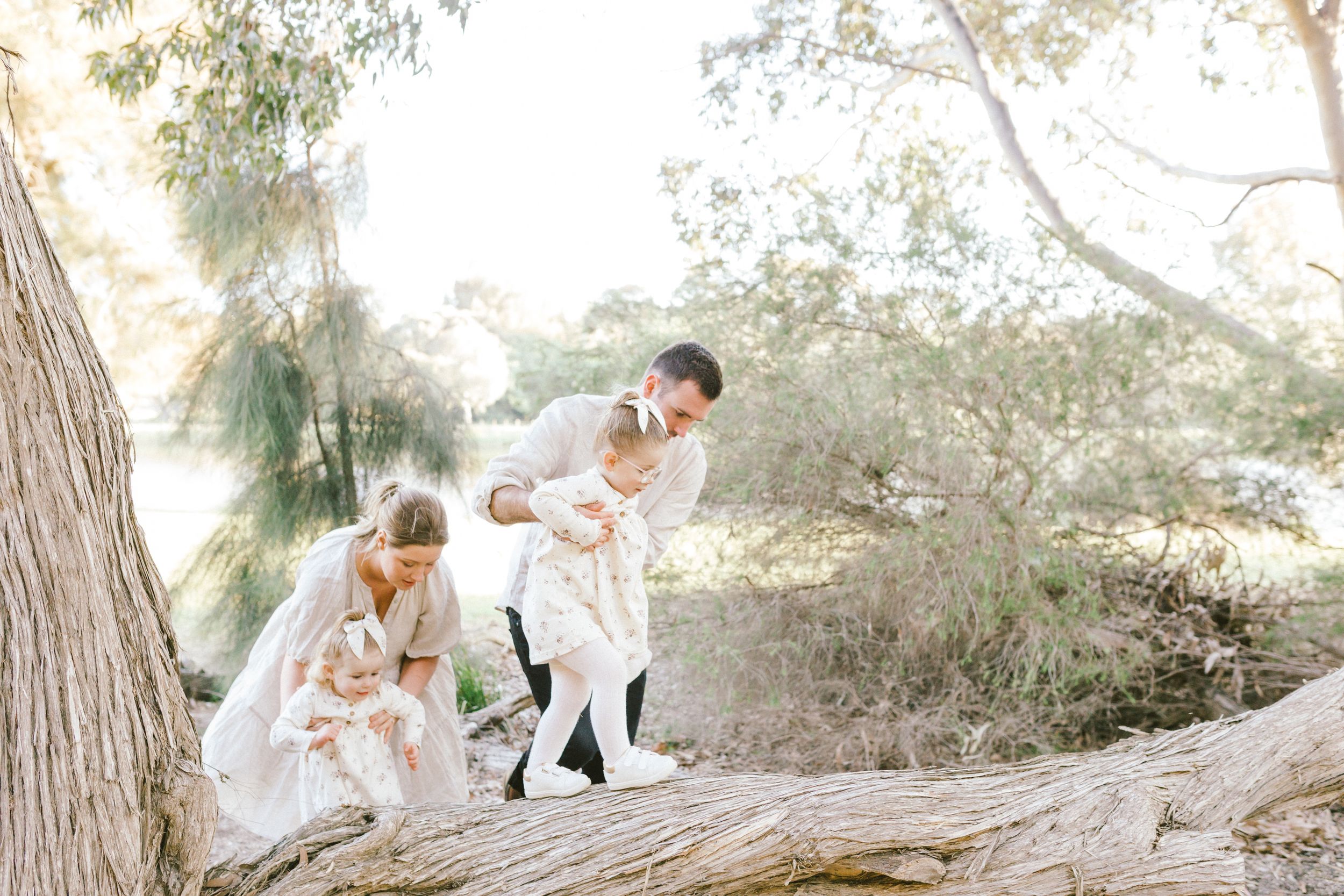 A romantic couple in white attire poses outdoors in a dreamy sunlit forest setting for wedding photos.