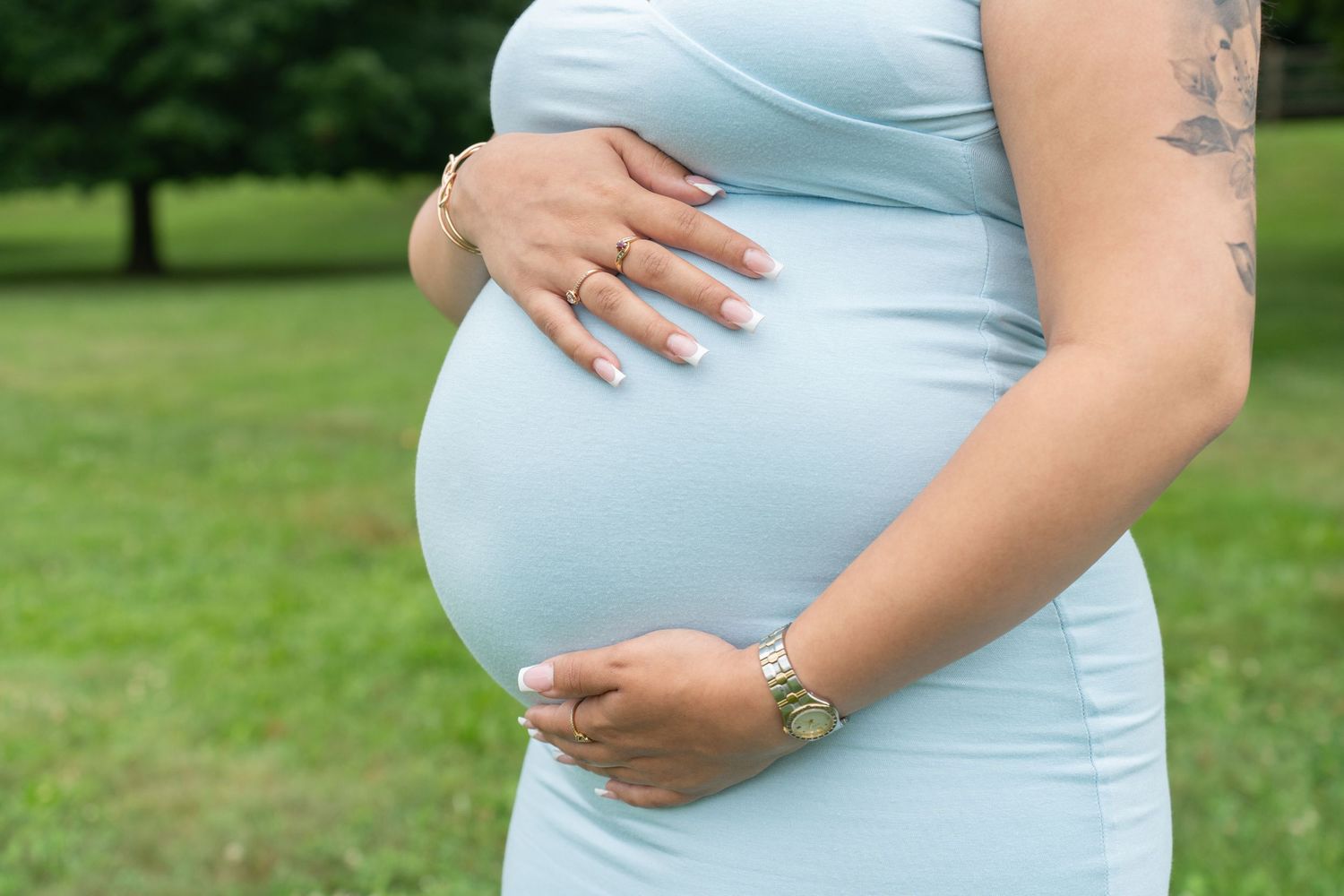 Close up of pregnant belly in light blue dress with hands gently resting on bump.