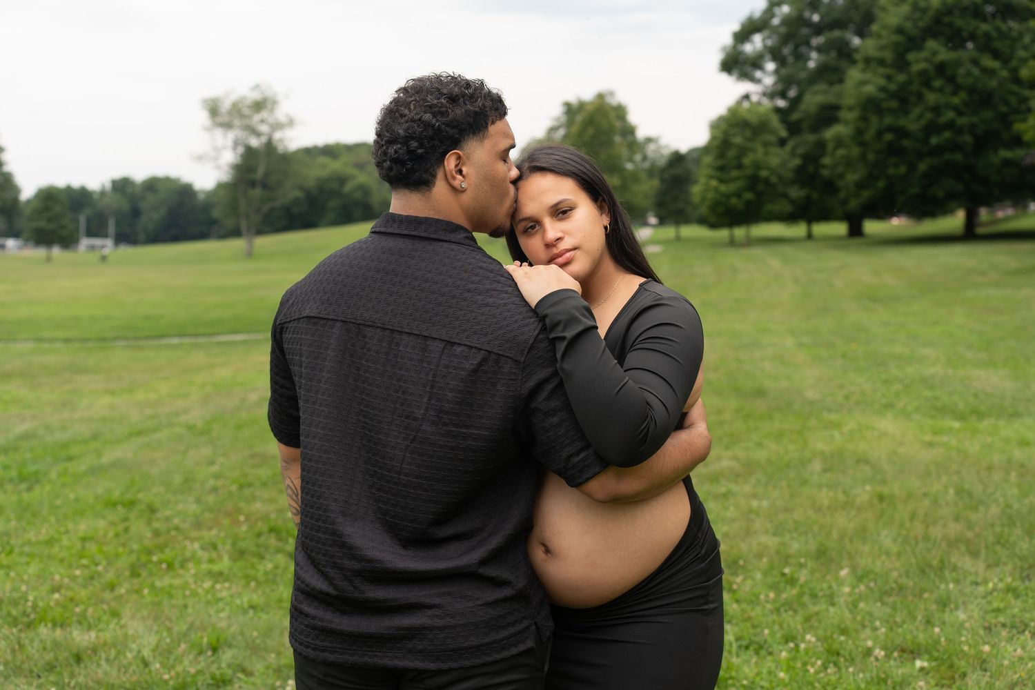Intimate maternity photo of couple embracing in a green field.