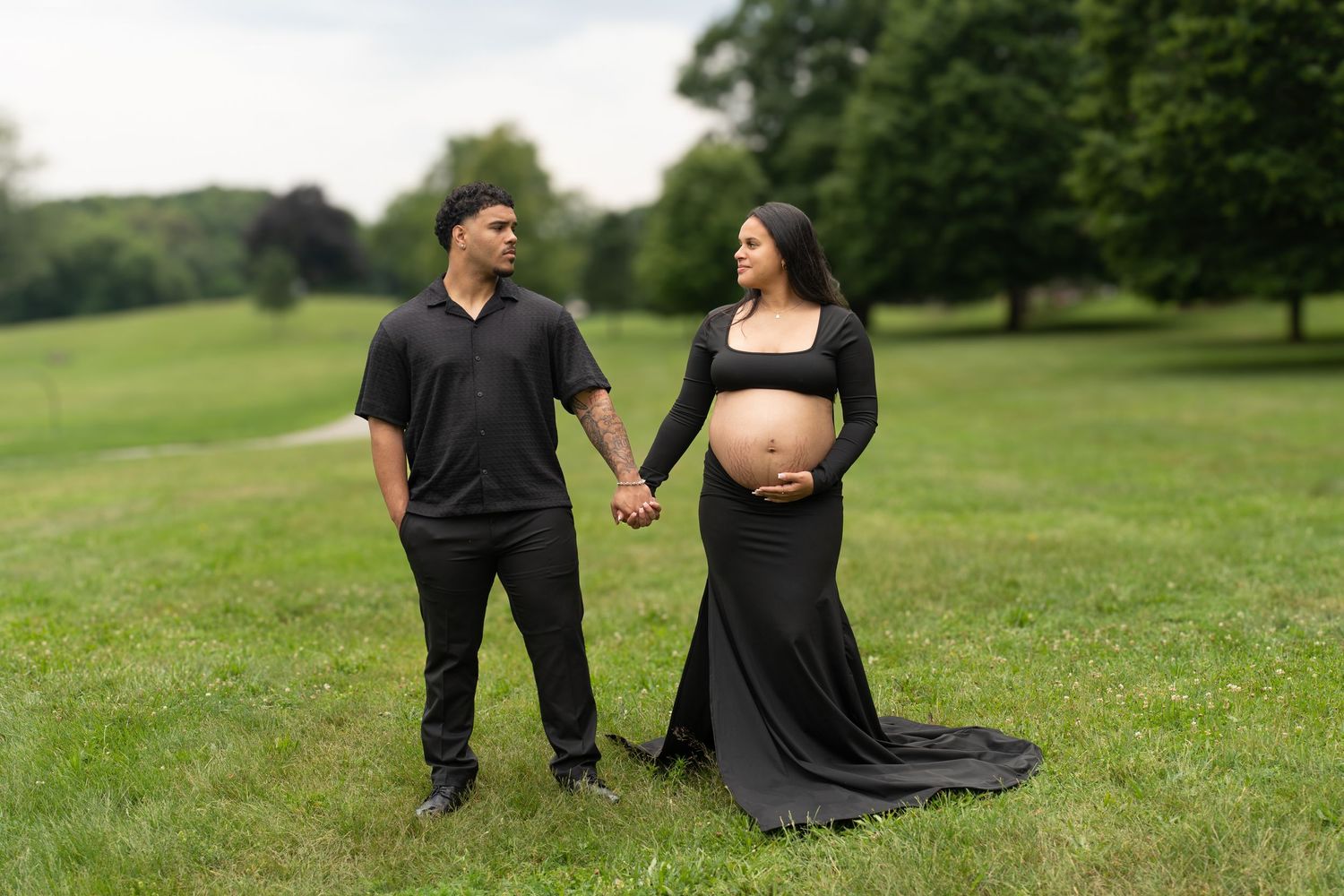 Expectant couple holding hands during outdoor maternity photoshoot in black attire.