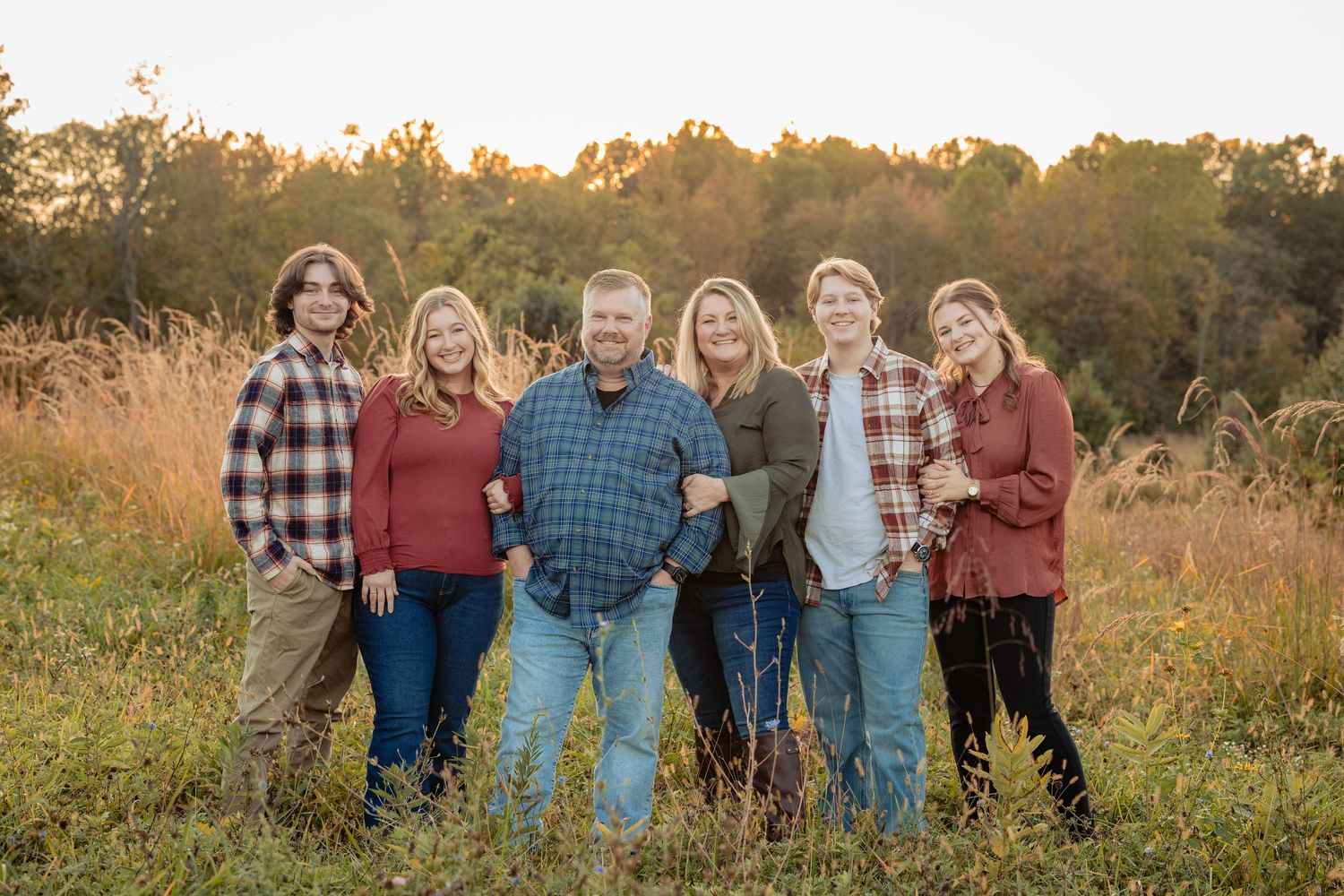 Group poses together in casual fall attire against golden sunset field with tall grass.