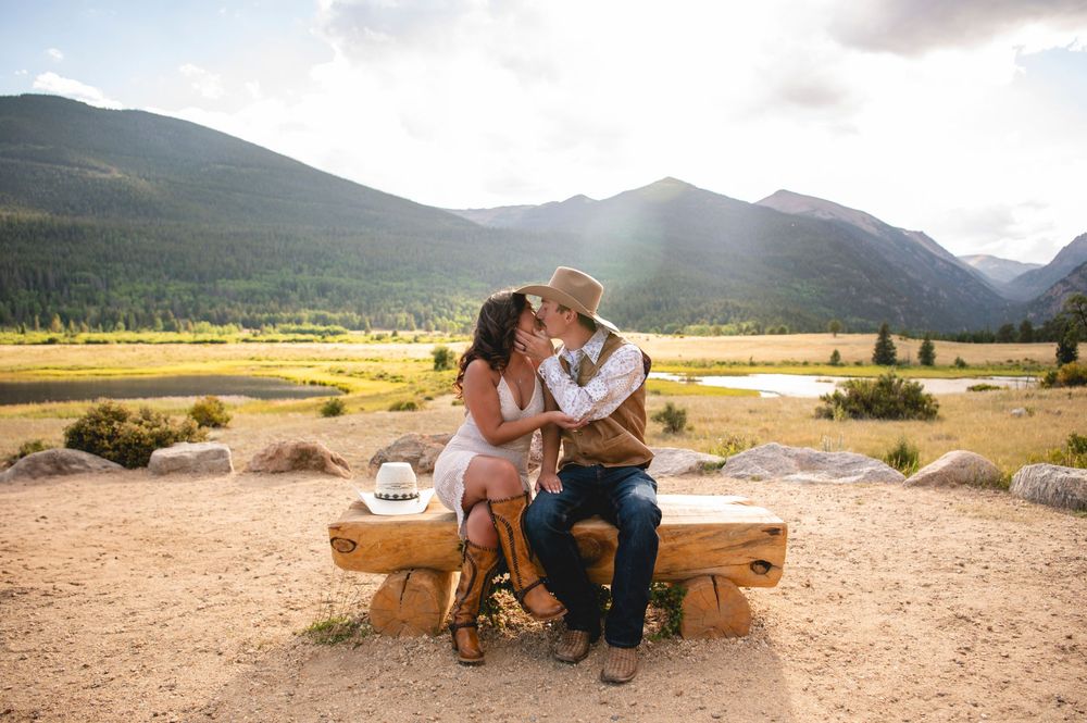 Romantic couple sitting on rustic wooden bench in scenic mountain meadow at sunset.