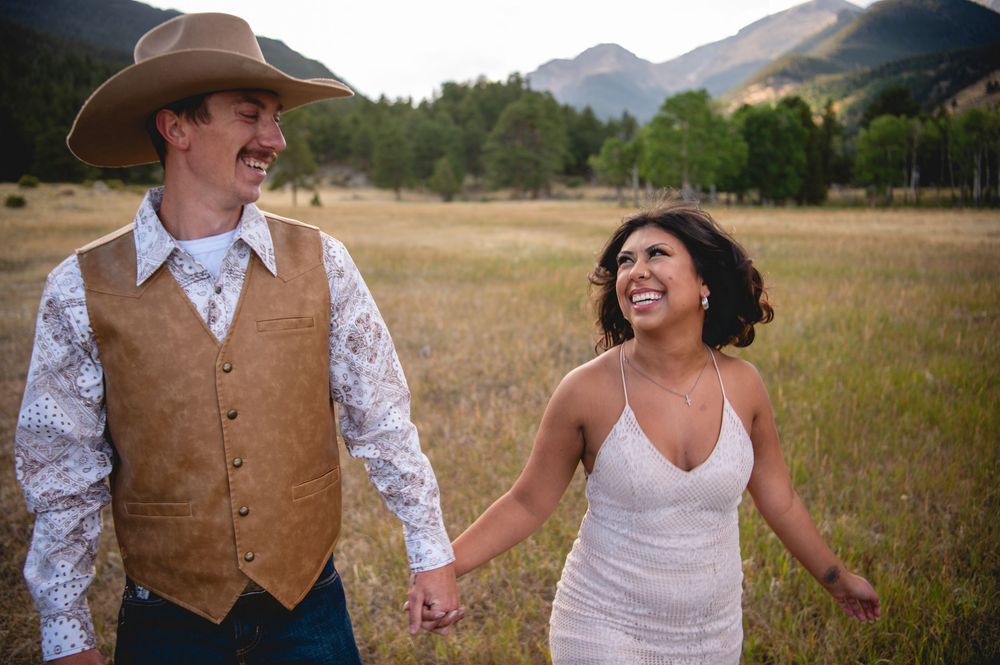 Happy wedding couple walking hand in hand through an open mountain meadow at sunset.