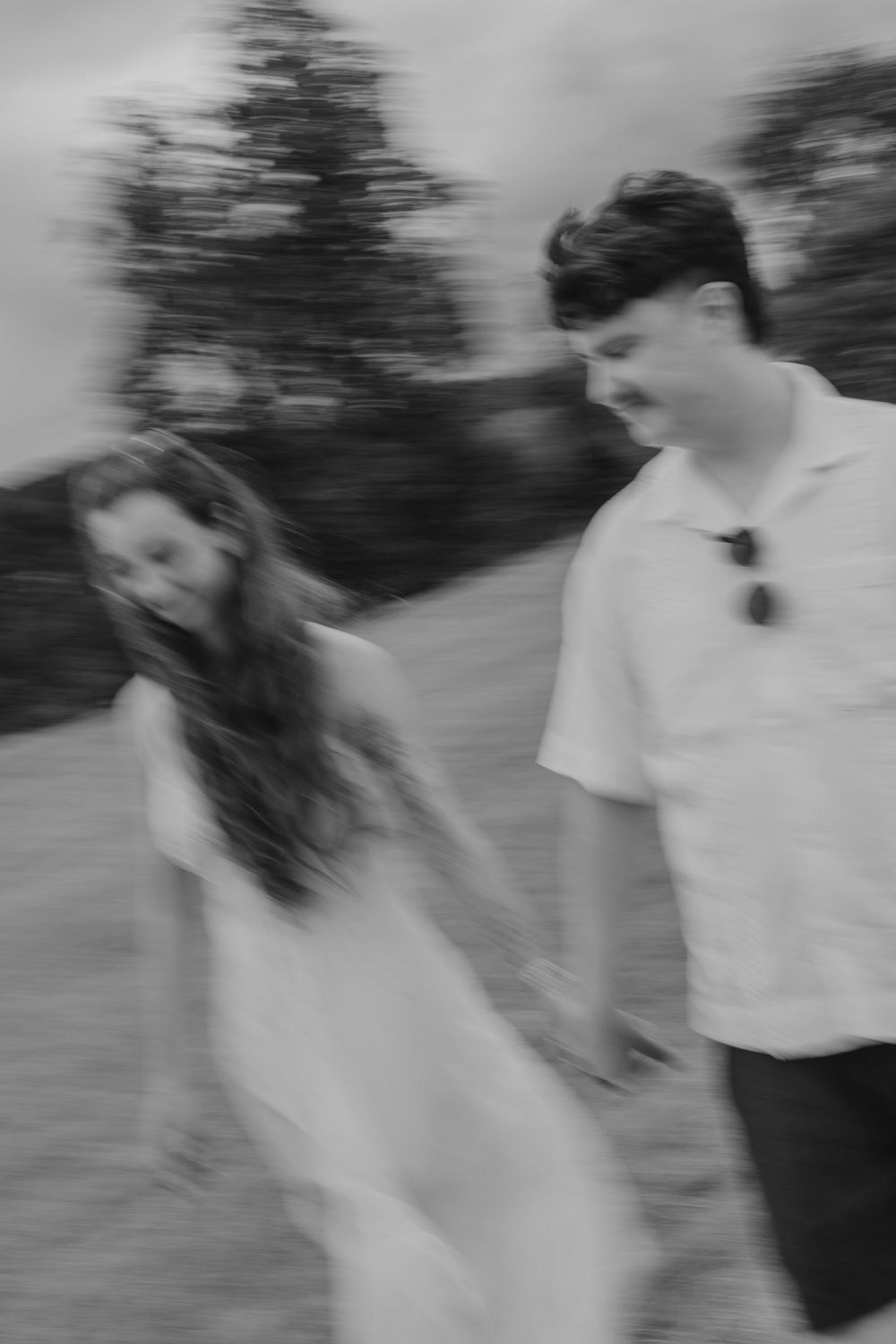 Black and white photo of a young couple holding hands and walking together outdoors in a field.