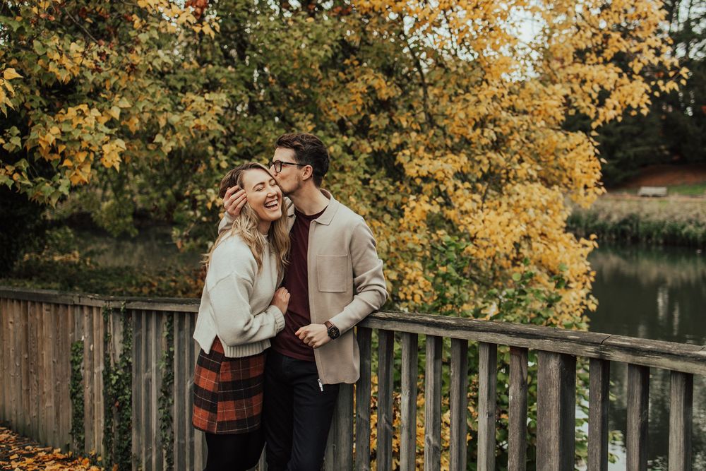 A couple embraces outdoors during autumn with golden yellow foliage in the background.