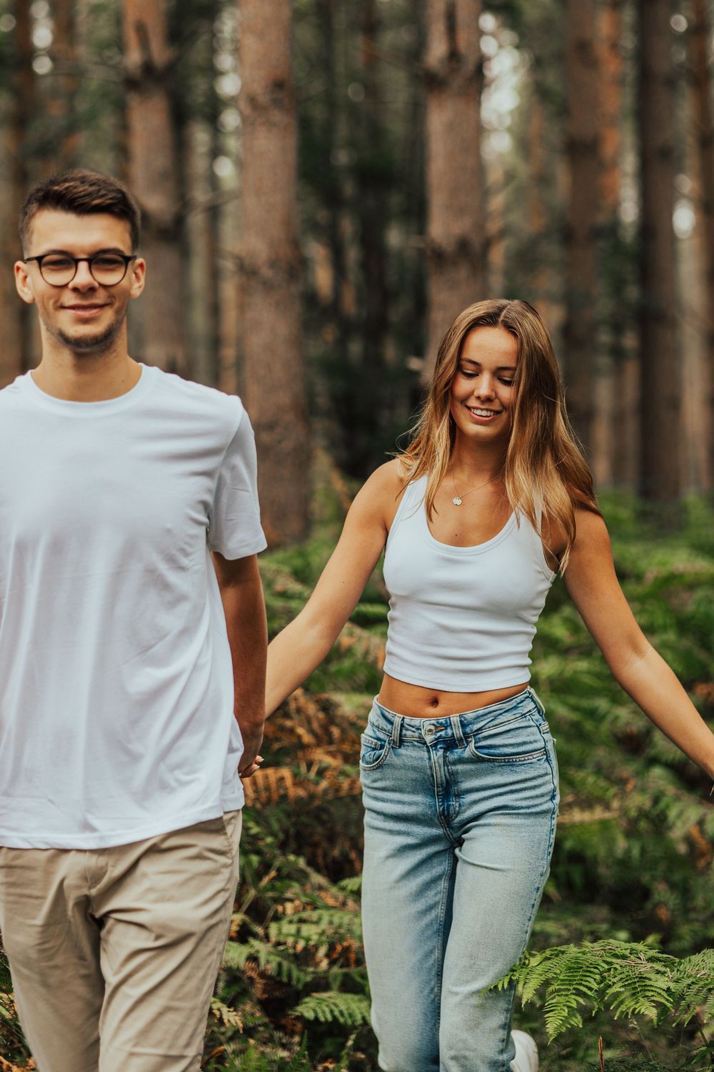 Group of friends in white t-shirts and jeans walking together through a sunlit pine forest.