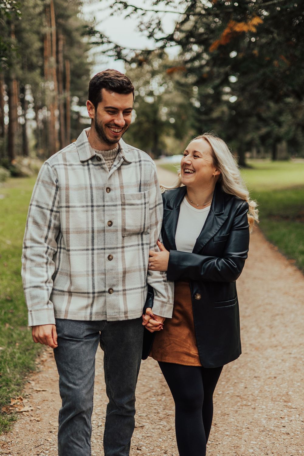 A couple walking hand in hand along a forest path while sharing a laugh on an autumn day.