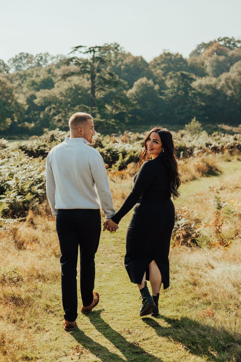 A couple walking hand in hand through a sunlit meadow during golden hour.