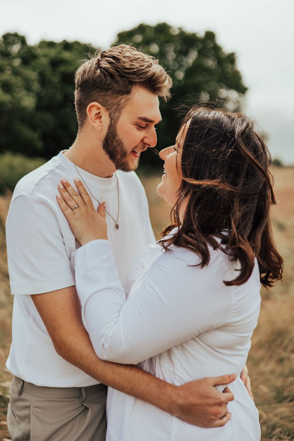 Romantic couple dressed in white embraces in a sunny field during sunset photo session.