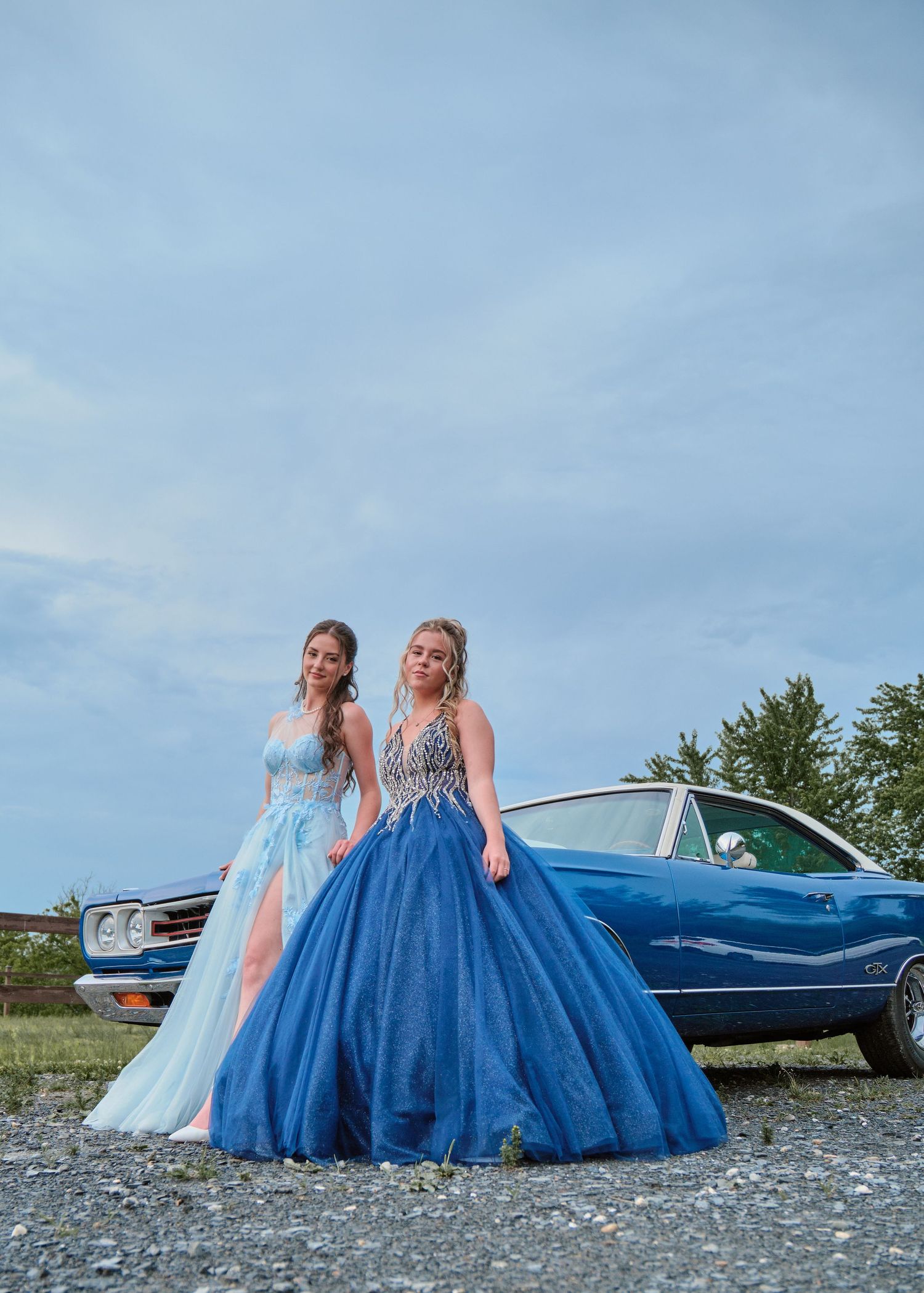deux jeunes femmes en tenues de soirée adossées à une voiture ancienne