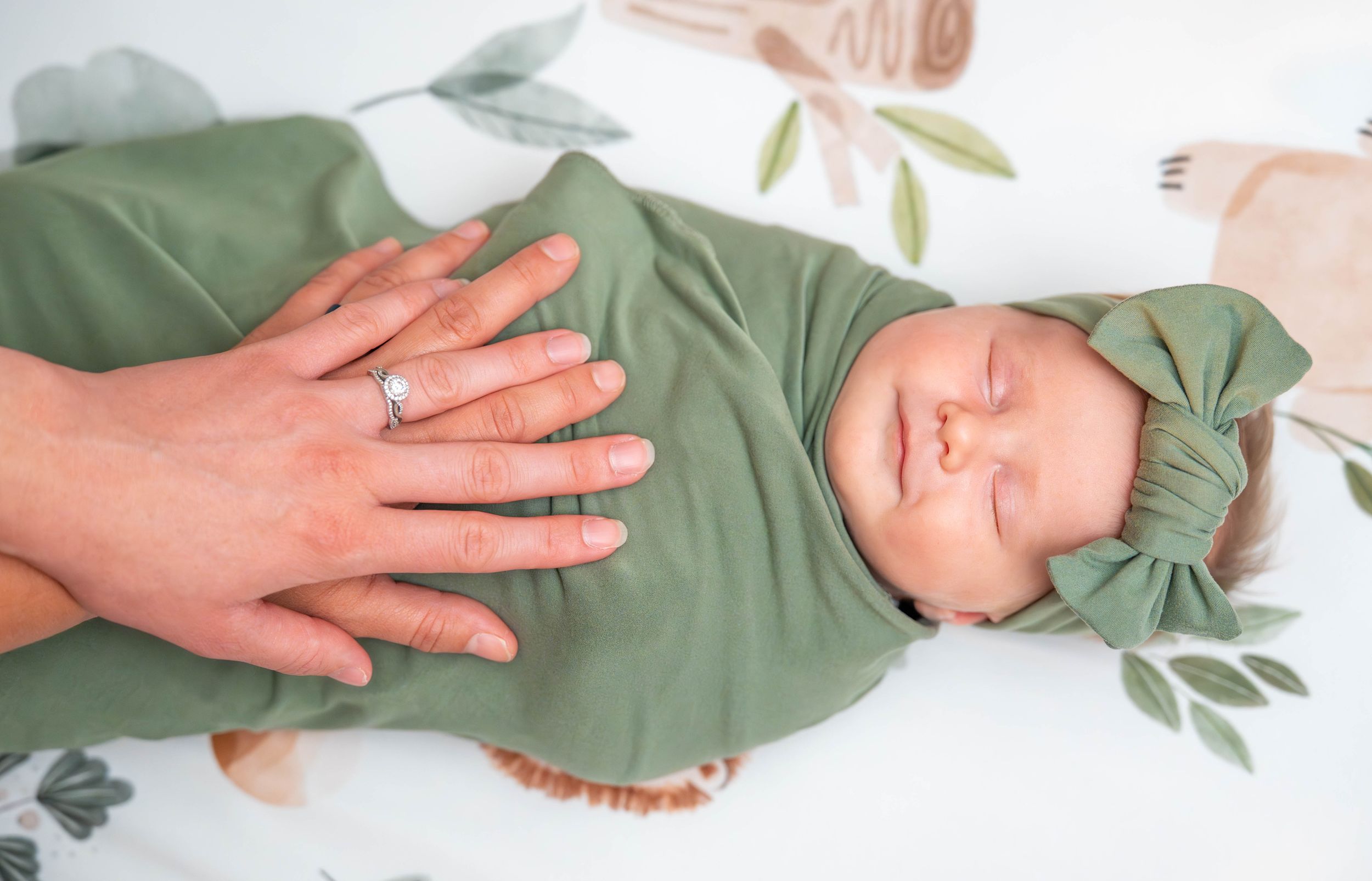 Adult hand rhythmically patting baby wearing green onesie to help soothe and calm. Quad Cities Newborn Photography