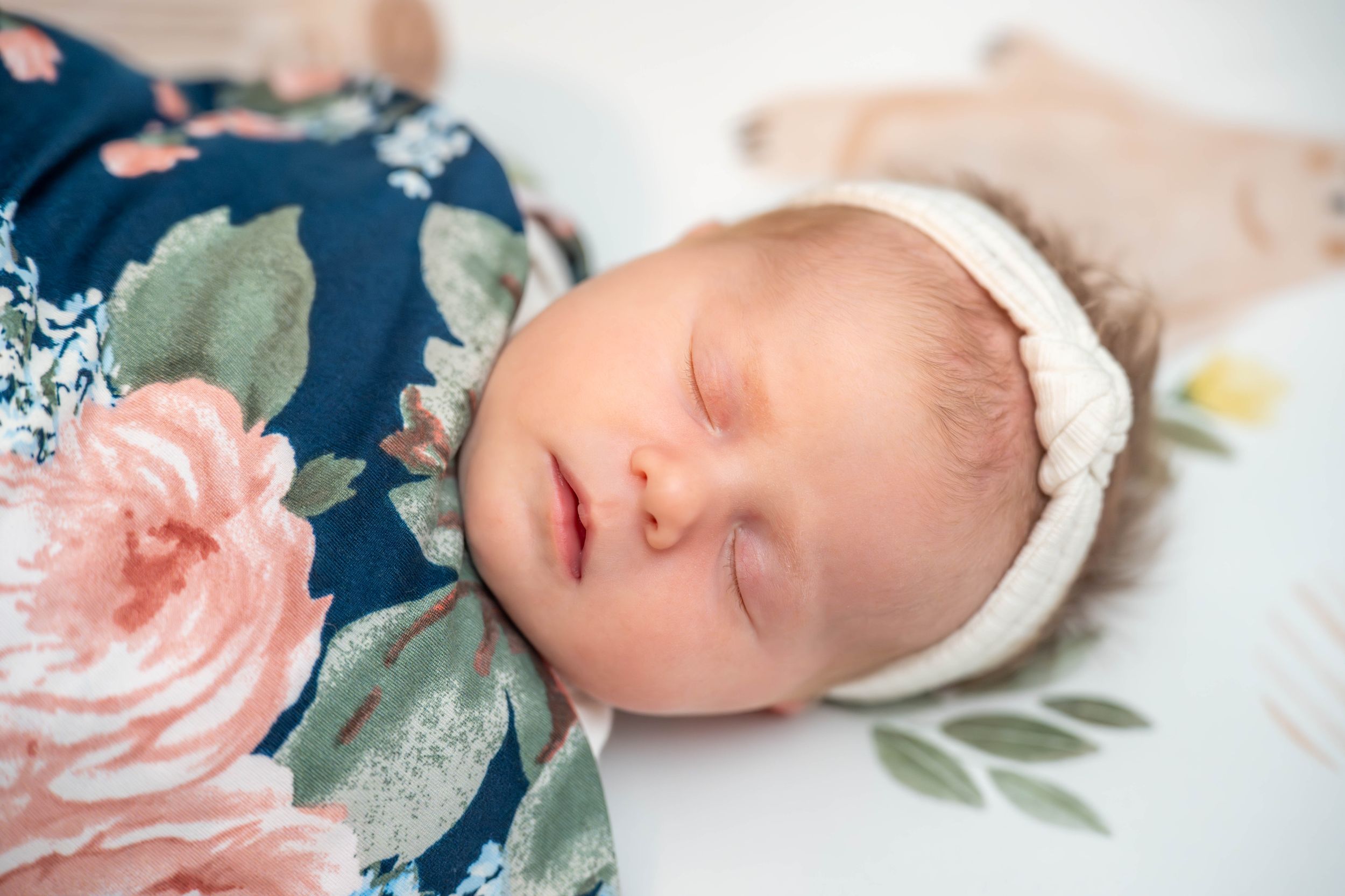 A sleeping newborn baby in olive green attire lays peacefully against a floral background. Quad Cities Newborn Photography