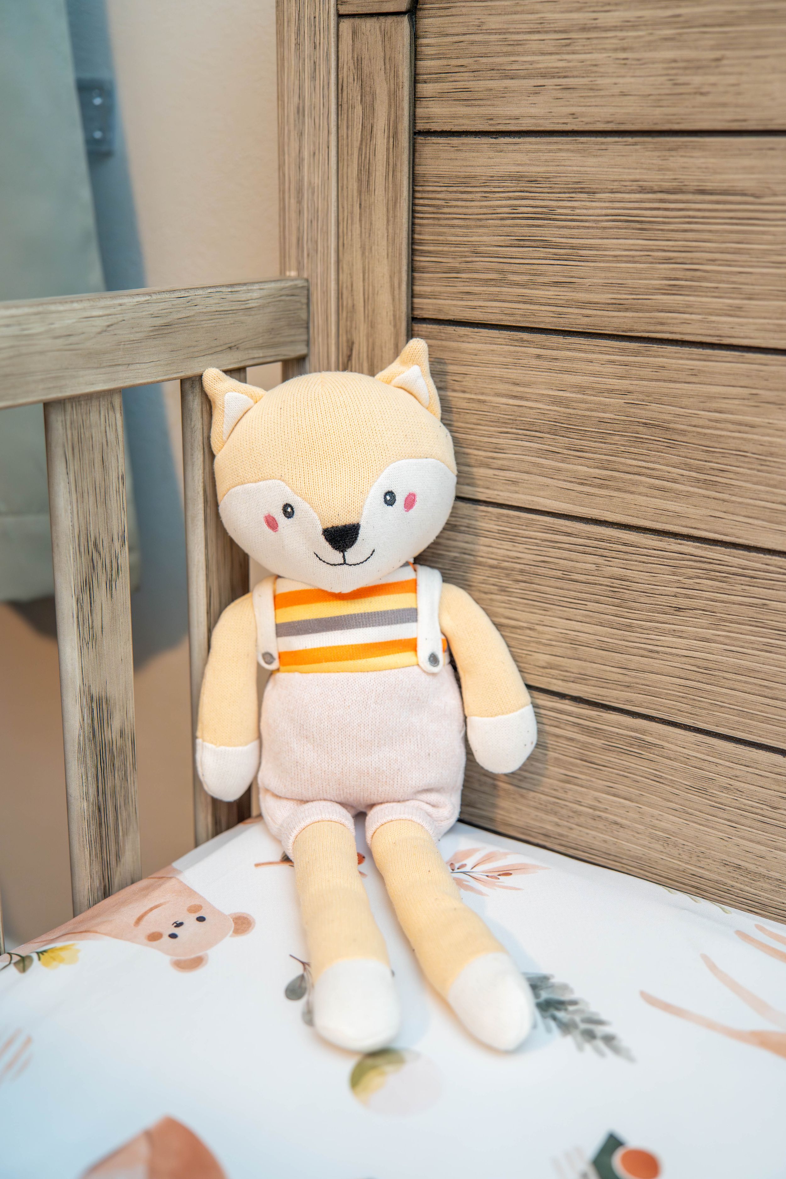 A plush toy fox with striped overalls sits against a wooden wall in soft lighting. Quad Cities Newborn Photography