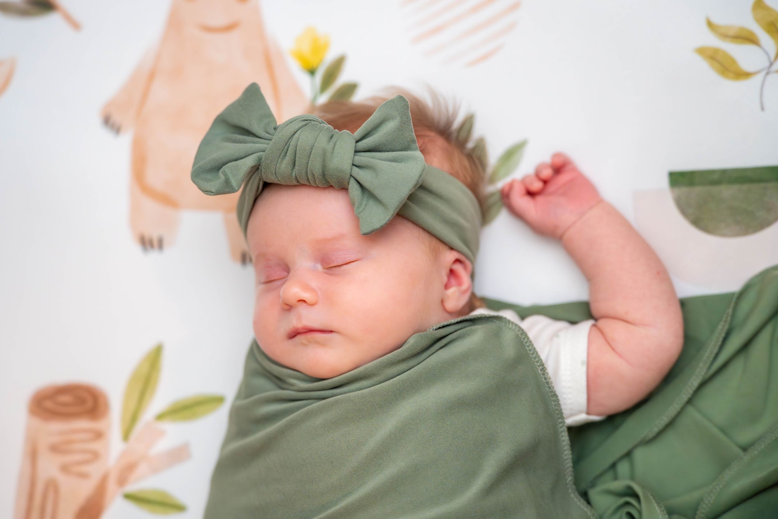 A baby in a sage green outfit rests on a white surface with delicate floral decor. Quad Cities Newborn Photography